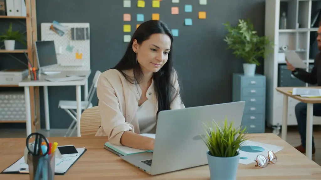 Travail hybride TPE PME - salariée travaillant sur ordinateur portable dans un bureau partagé.